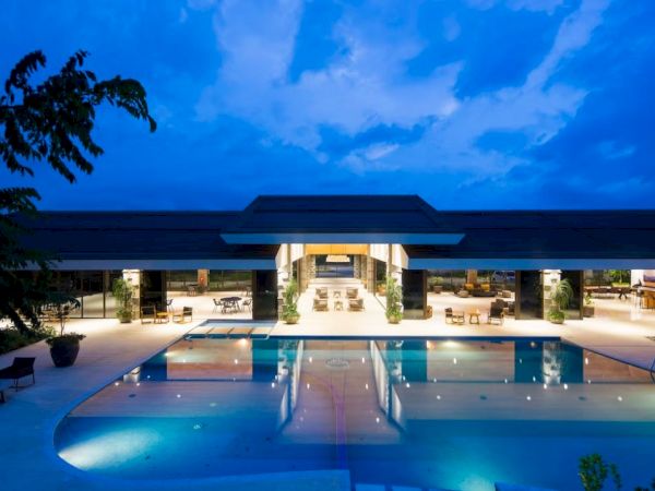 A luxurious outdoor pool area with modern architecture, well-lit at dusk, featuring a large pool surrounded by lounge seating and greenery.