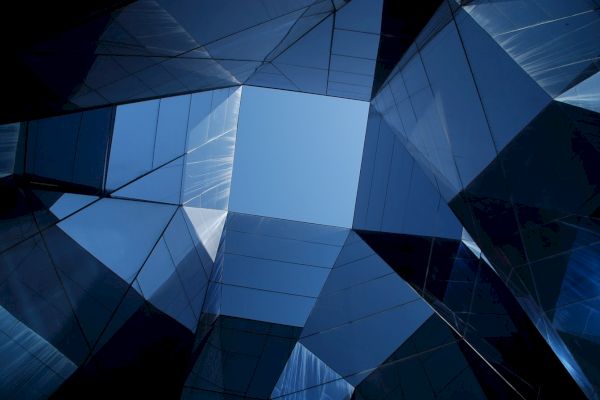 The image shows a geometric pattern created by glass-covered buildings or structures, with a view of the sky at the center.