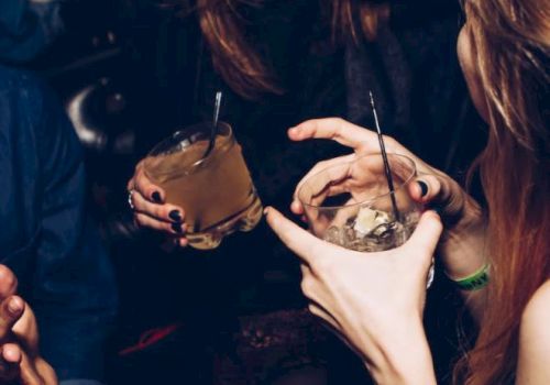 People are holding drinks and socializing at what appears to be a lively gathering or party, engaging in conversation and enjoying themselves.