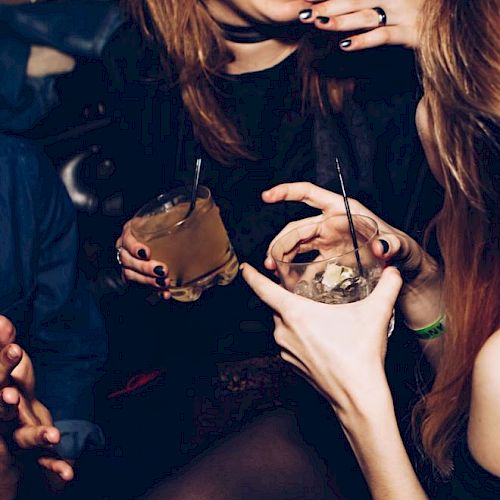 People are holding drinks and socializing at what appears to be a lively gathering or party, engaging in conversation and enjoying themselves.