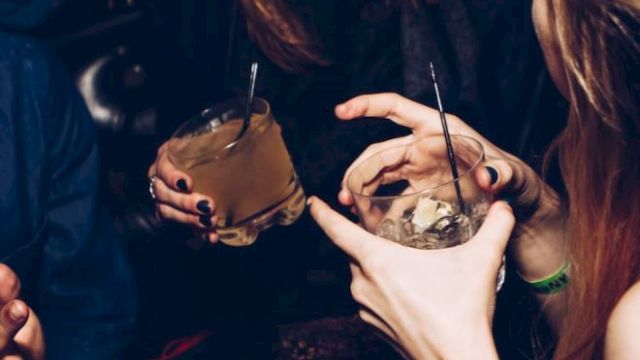 People are holding drinks and socializing at what appears to be a lively gathering or party, engaging in conversation and enjoying themselves.