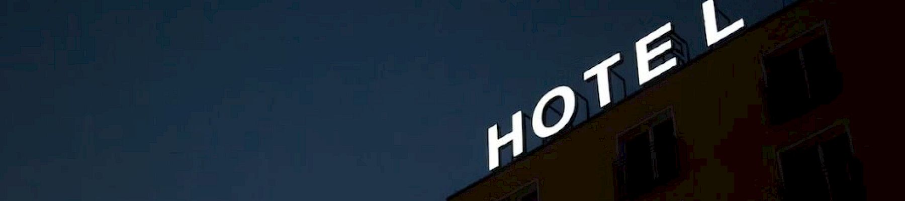A building at dusk features a partially lit "HOTEL" sign, with the letter "T" in the hotel's sign non-illuminated.