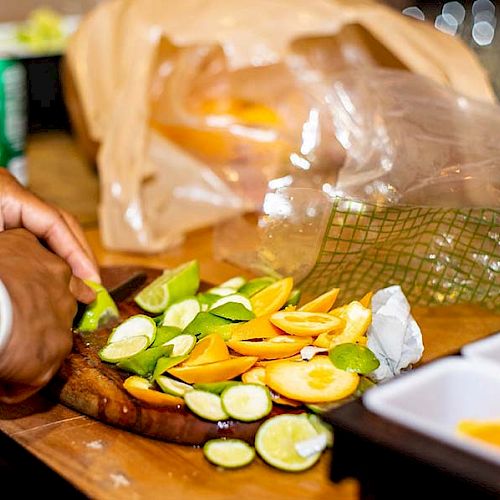 A person is slicing various citrus fruits, including lemons and limes, on a cutting board with other kitchen items and a can in the background.