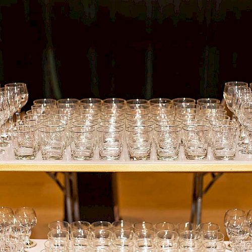 The image shows multiple rows of empty glasses neatly arranged on a table, likely prepared for an event or gathering.