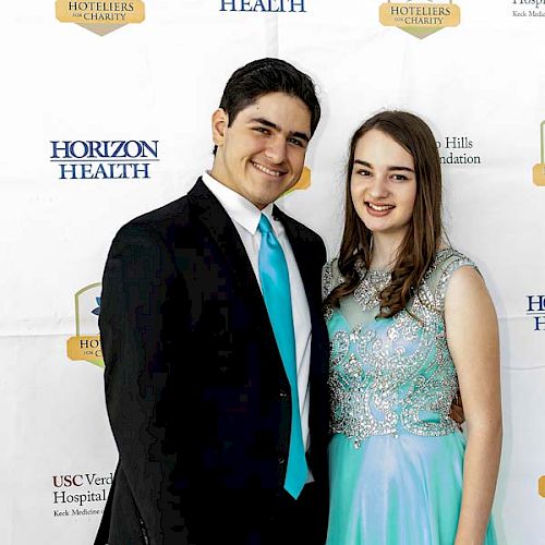 A young man in a suit and a young woman in a light blue dress pose together in front of a Horizon Health backdrop.