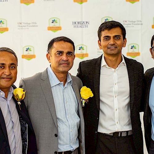 The image shows four men standing together at an event with Horizon Health branding in the background. Each man has a yellow rose corsage.