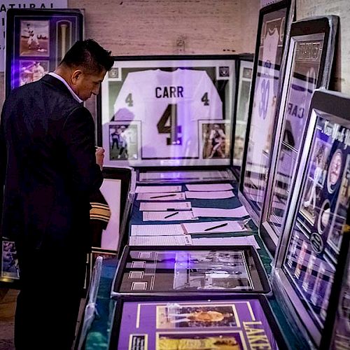 A man at an exhibit examines framed sports memorabilia including jerseys, photographs, and documents.