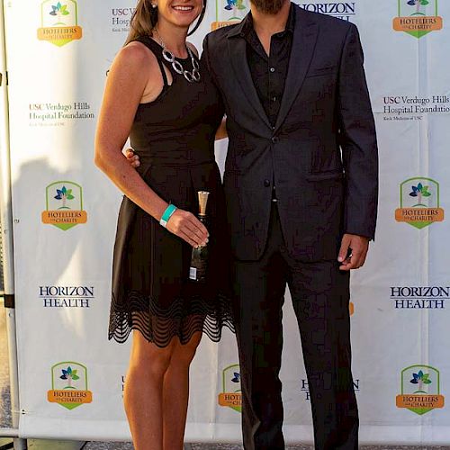 A man and a woman are dressed formally, posing for a photo with a backdrop displaying logos from Horizon Health and Unexpected Wildlife Refuge.