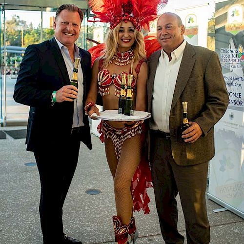 Three people: Two in suits holding drinks, and one in a showgirl costume with a feathered headdress, holding a drink tray.