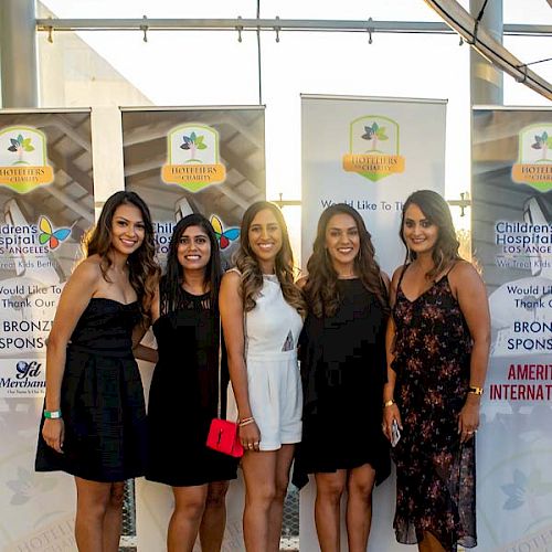 A group of five women posing together indoors, standing in front of banners and what appears to be a large skeleton structure.