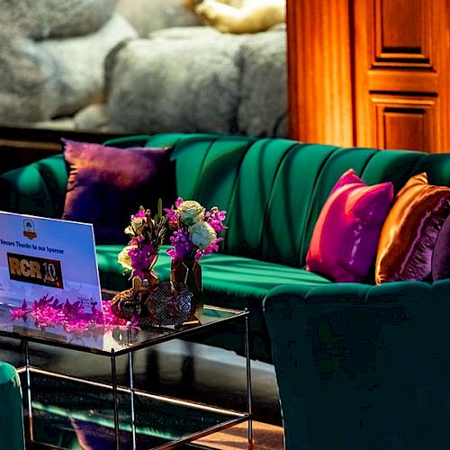 A plush green sofa with colorful pillows, a glass table with flowers, candles, and a sign in a cozy, warmly lit room.