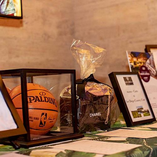 The image shows framed sports jerseys, a basketball in a display case, a Chanel item, and certificates on a table.