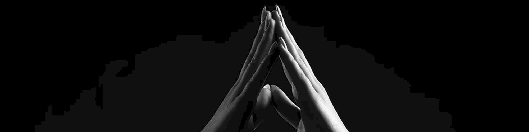 Two hands meeting fingertips in a gesture akin to prayer or connection, contrasting sharply against a dark background, creating a poignant visual.