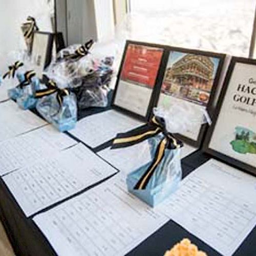 The image shows a table displaying gift bags, framed signs, and documents, possibly at an event registration or prize booth, with a 