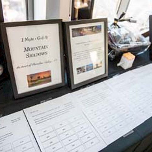 The image shows a table with displayed items, including framed documents, various papers for a silent auction, gift baskets, and baseball memorabilia.