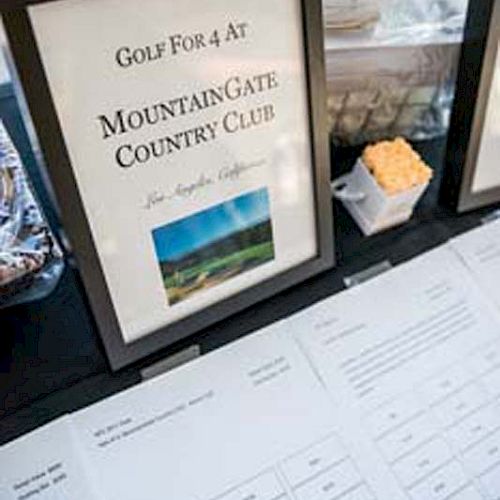 A framed sign for a golf outing at MountainGate Country Club, Los Angeles, alongside raffle prize entry sheets on a table.