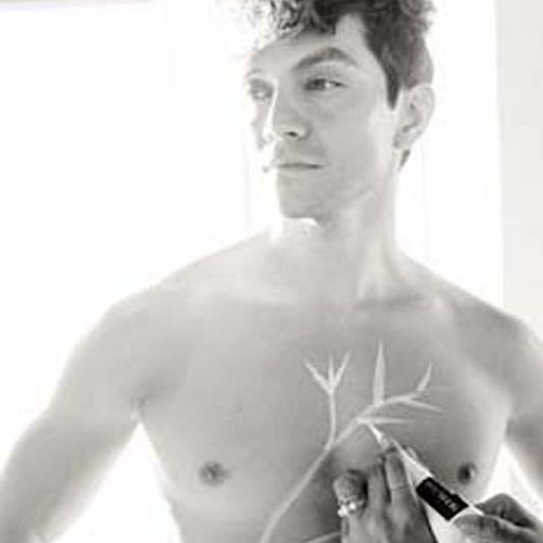 A shirtless person is having a design drawn on their chest with a marker, featuring an artistic branching pattern.