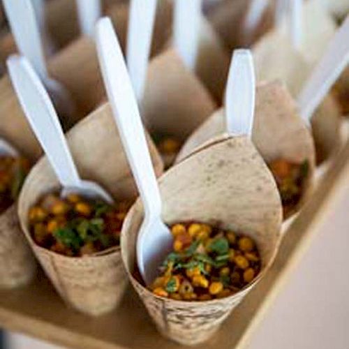 The image shows several cone-shaped containers filled with a corn-based dish, each with a plastic spoon placed inside the cone.