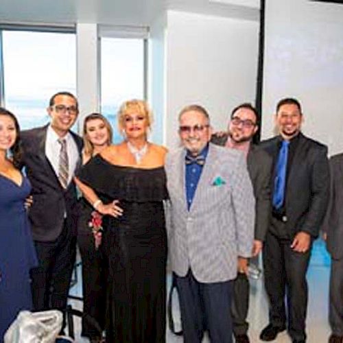 A group of people dressed in formal attire posing together in a room with large windows.