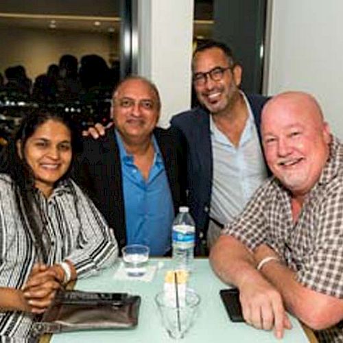 A group of four people smiling at a table with drinks and a city view in the background.