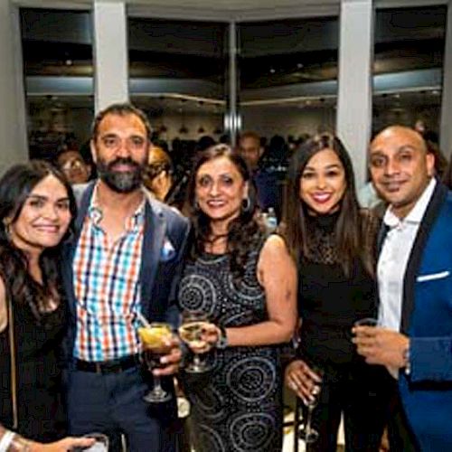 A group of five people, dressed in formal attire, are posing for a photo at an event or party.