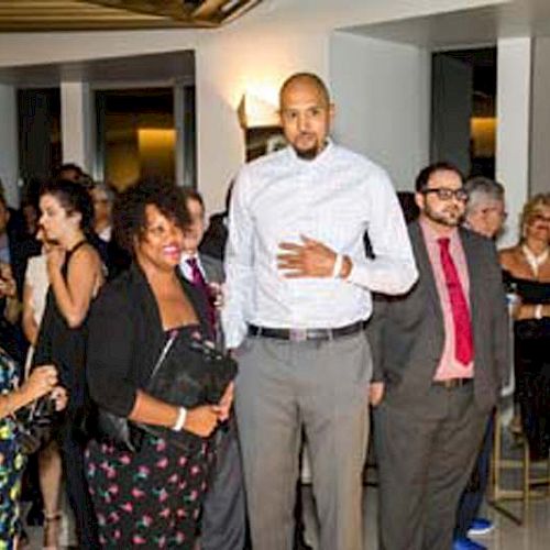 A group of people, dressed in formal attire, are gathered at an indoor event, smiling and conversing with each other.