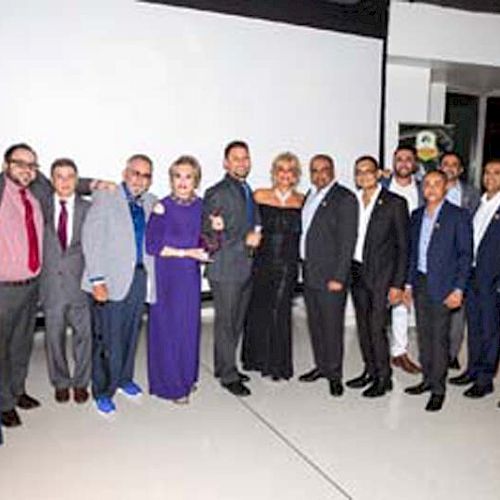 A group of people dressed in formal attire posing together in front of a large screen in a modern setting, all smiling for the photo.