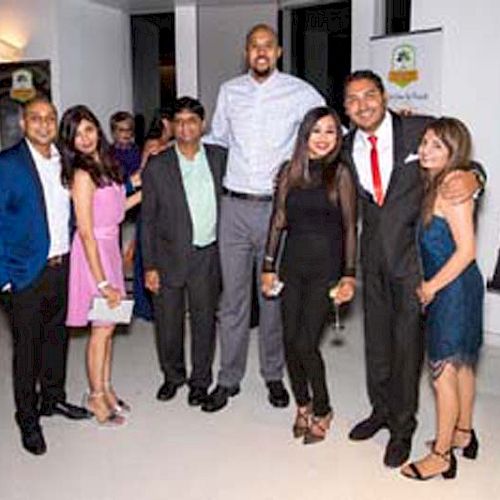 A group of people are posing for a photo at what appears to be a formal event, dressed in semi-formal to formal attire.