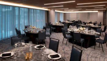 This image shows an elegant dining venue with several round tables set for a formal event, featuring blue chairs, glassware, and floral centerpieces.