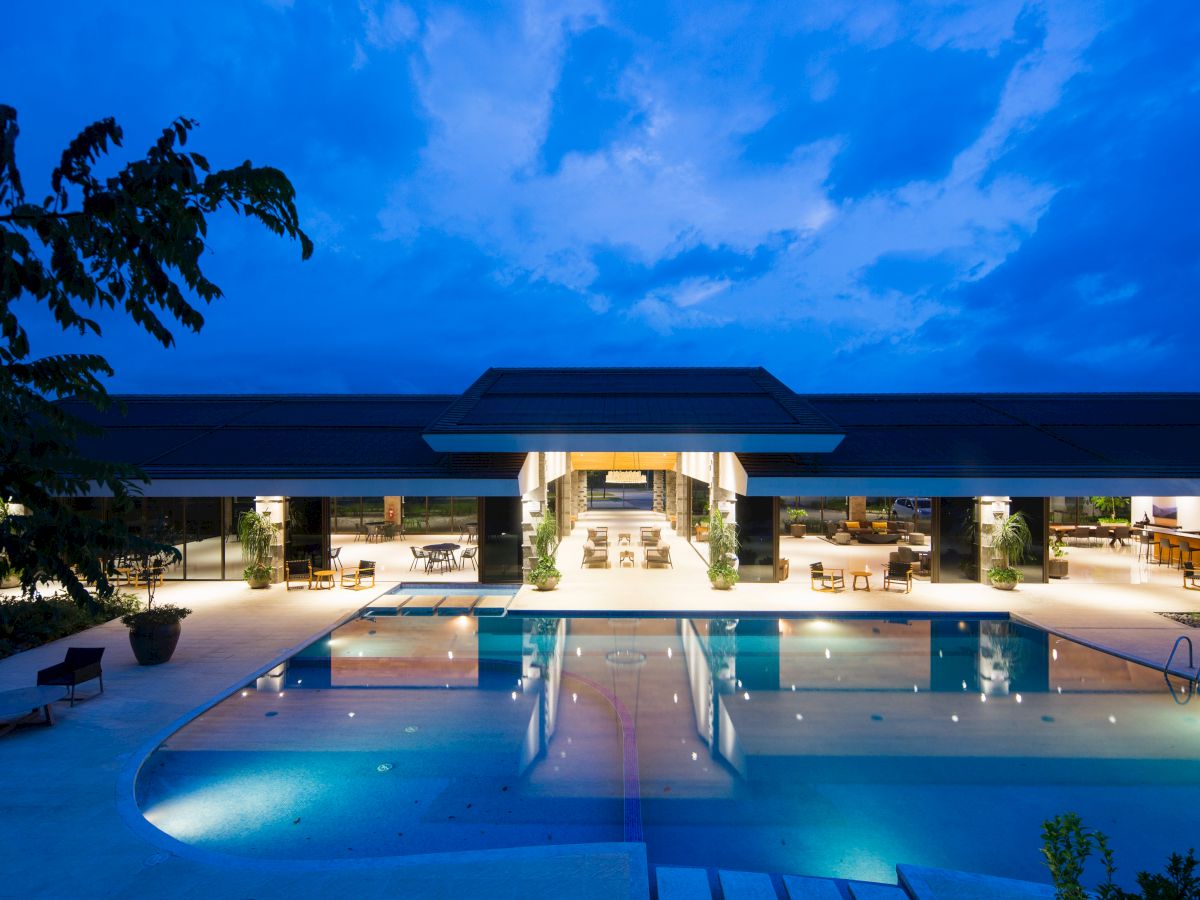 A modern building with an illuminated swimming pool, open seating areas, and a clear night sky in the background always ending the sentence.