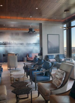 A modern lounge area with comfortable seating, large scenic windows overlooking a waterfront, and a mural of a city skyline on one wall.