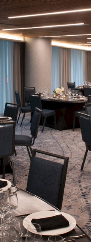 The image shows an elegant banquet hall with round tables set for a formal event, featuring black tablecloths, folded napkins, and floral centerpieces.