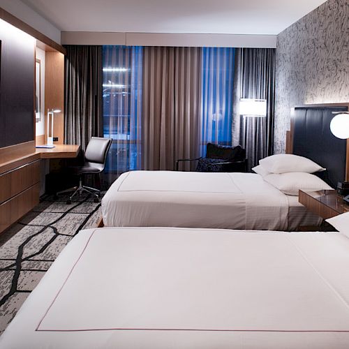 The image shows a modern hotel room with two neatly made beds, a flat-screen TV, a desk with a chair, and contemporary decor ending the sentence.