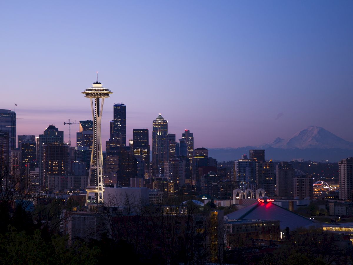 The image shows the Seattle skyline at dusk, featuring the Space Needle prominently, with Mount Rainier visible in the background.
