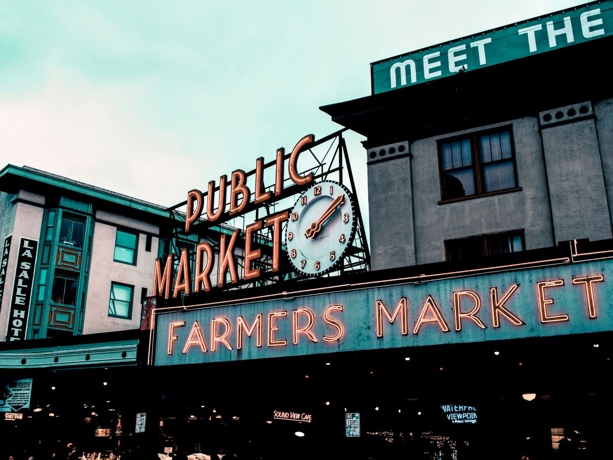 This image shows the iconic neon signs for the Public Market and Farmers Market at Pike Place Market in Seattle, with adjacent buildings in the background.